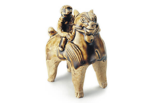 唐代．長沙窯青釉獅+青釉獅子四肢站立，昂首挺胸，睜大圓眼注視前方，背上馱負一人，模樣天真可愛。（圖二）